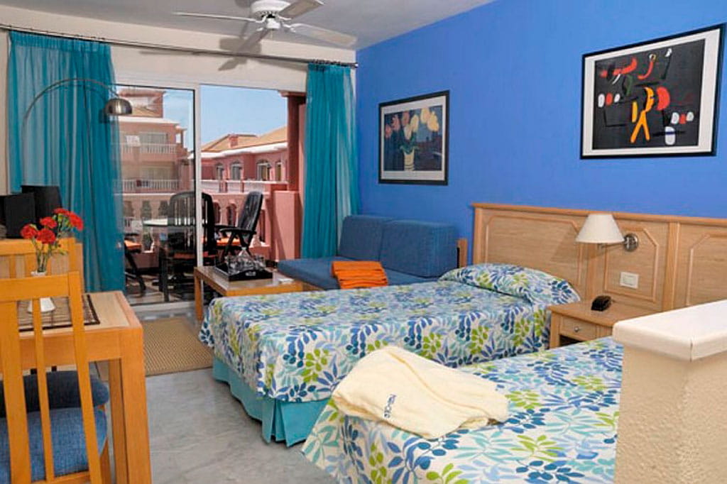 Room in Tenerife with twin beds, blue walls, artwork, and balcony view.