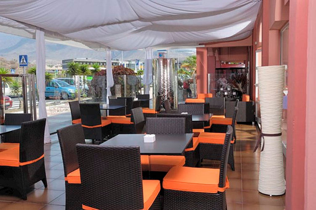 Outdoor dining area with orange-cushioned chairs and tables in Tenerife.