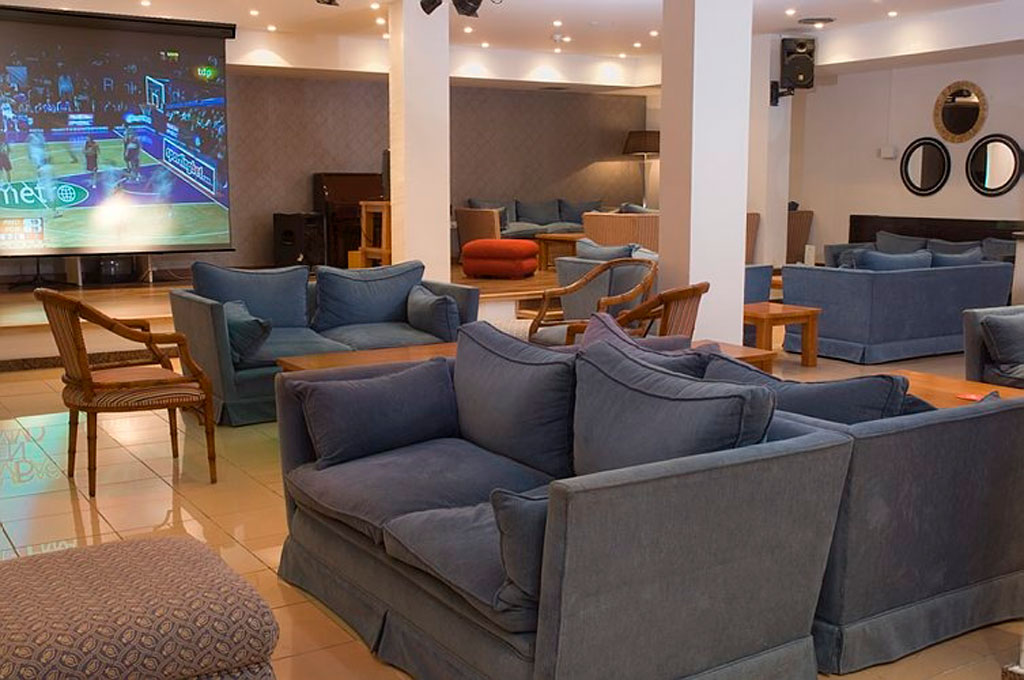 Seating area with sofas facing a large screen showing a basketball game in Tenerife.