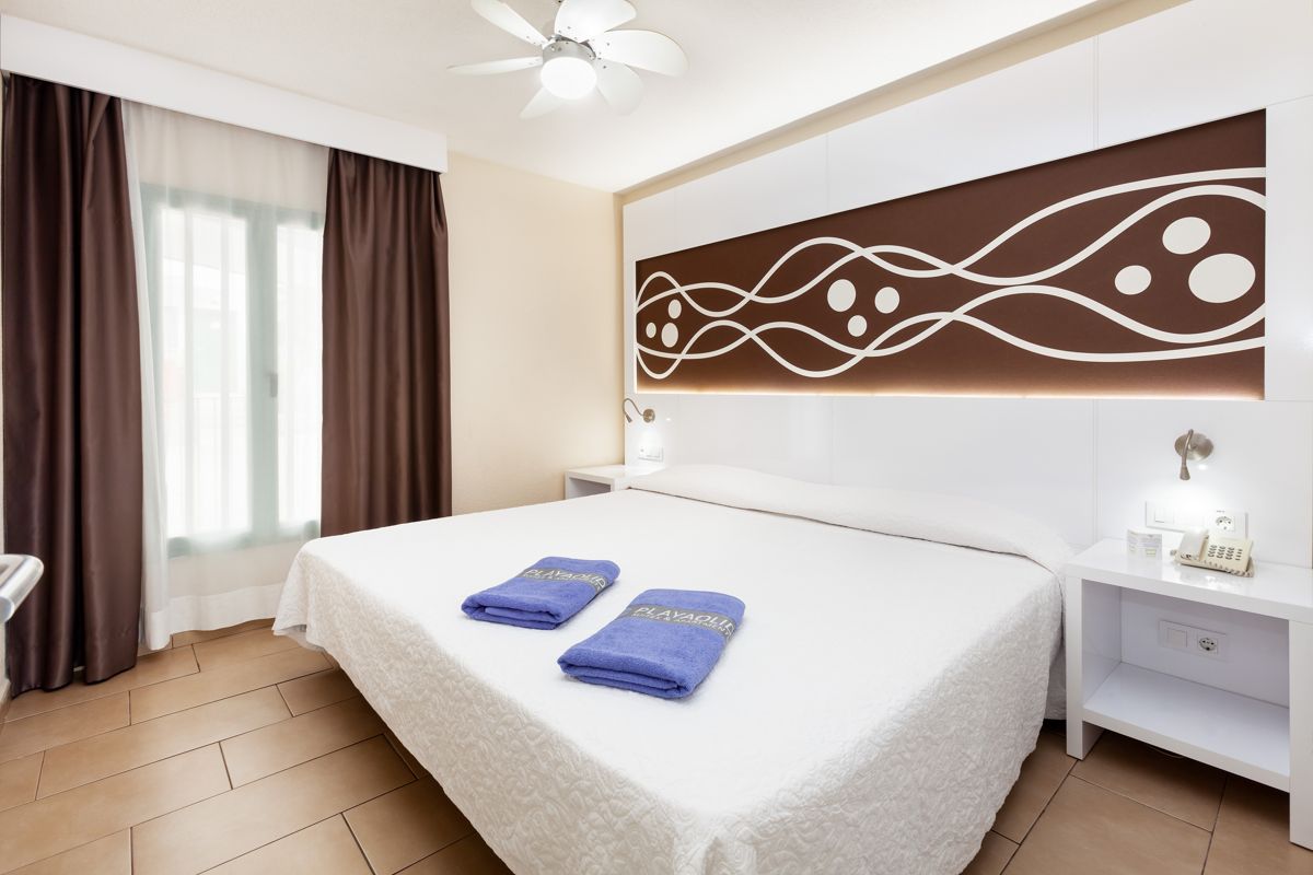 Modern decor bedroom in Tenerife hotel with king-size bed and lamps. Towels labeled Playaolid.