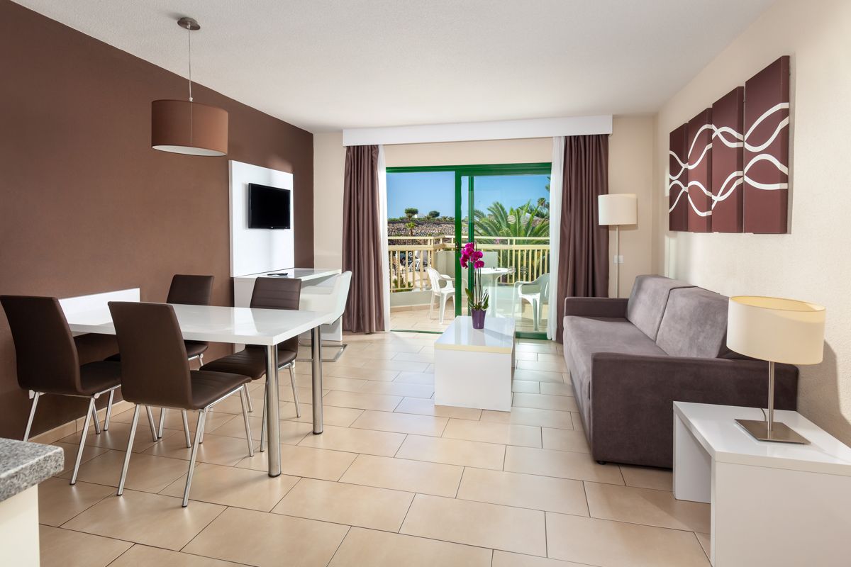 Living room with brown sofa, dining table, and balcony view in Tenerife.