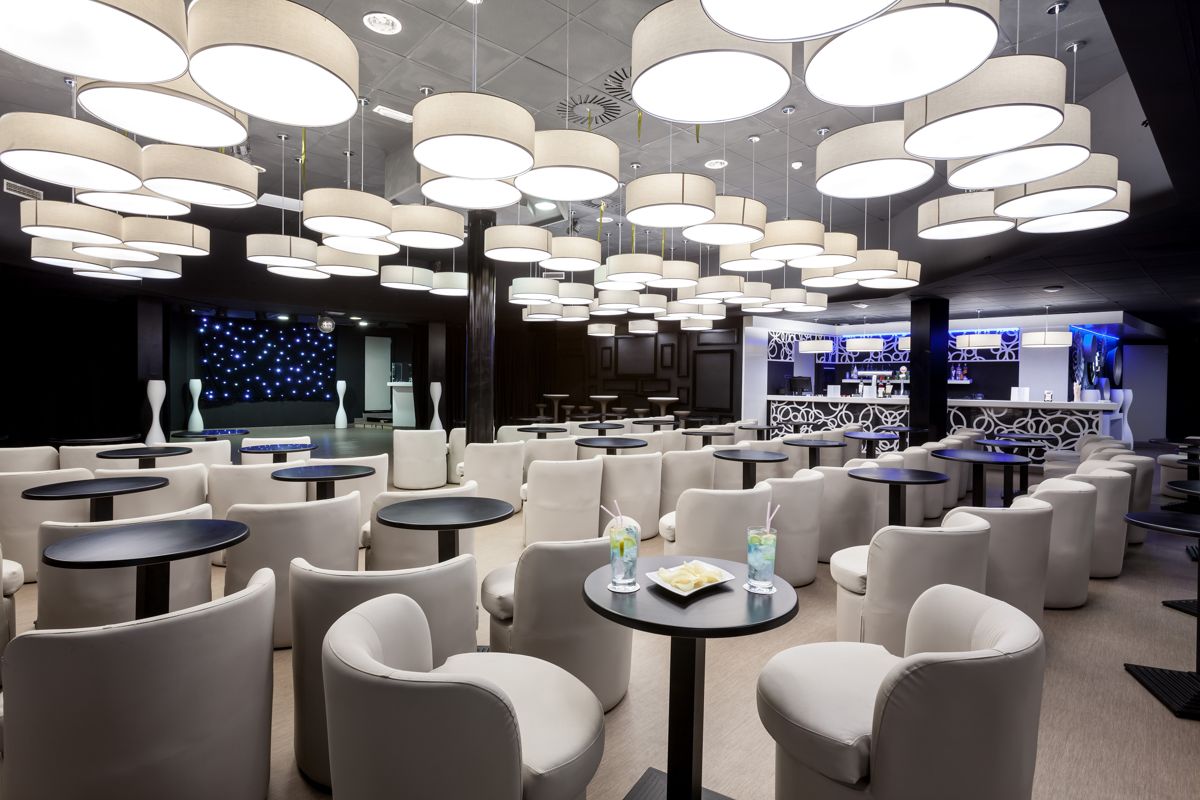 Lounge area in Tenerife with round tables, white chairs, and illuminated ceiling.