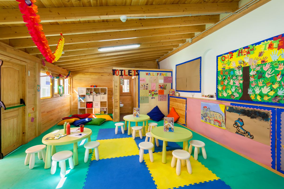 Colorful classroom with round tables, art on walls, and cushions in Tenerife. Text: TOILETS, WALL OF FAME.