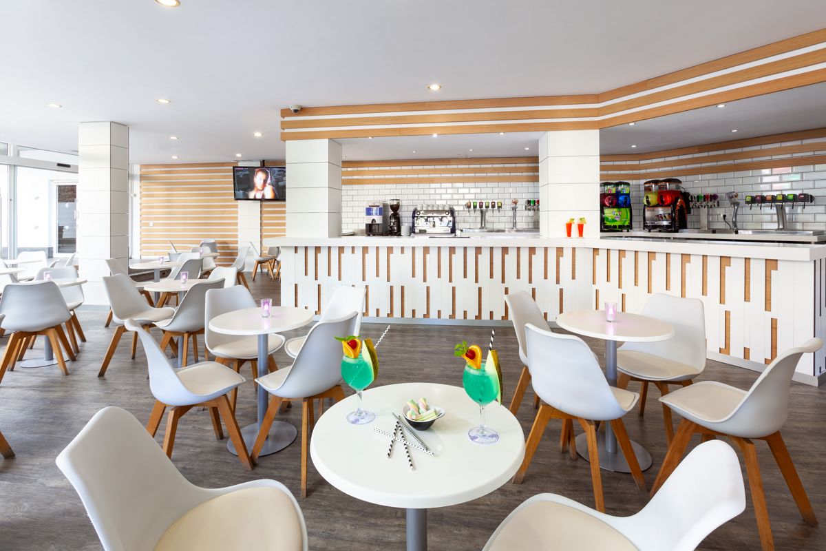 Modern coffee shop in Tenerife with white tables and chairs, serving blue cocktails.