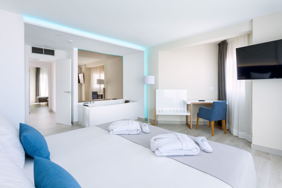 Modern hotel room in Tenerife with a bed, TV, desk, and natural light.