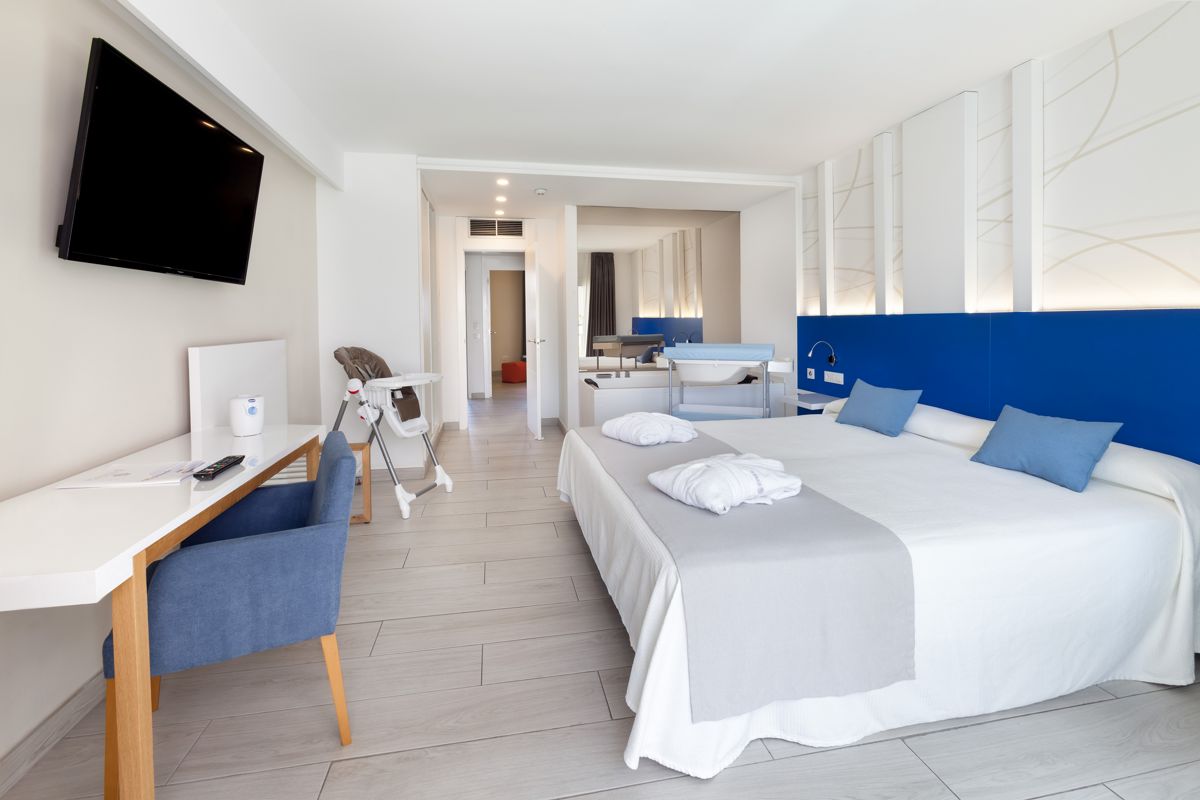 Double room with a TV, desk, and high chair in Tenerife hotel.