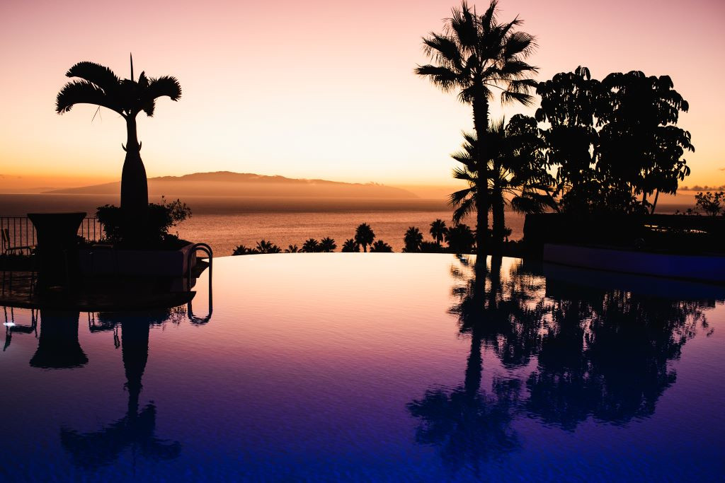 Sunset view with palm trees and ocean from a pool in Tenerife.