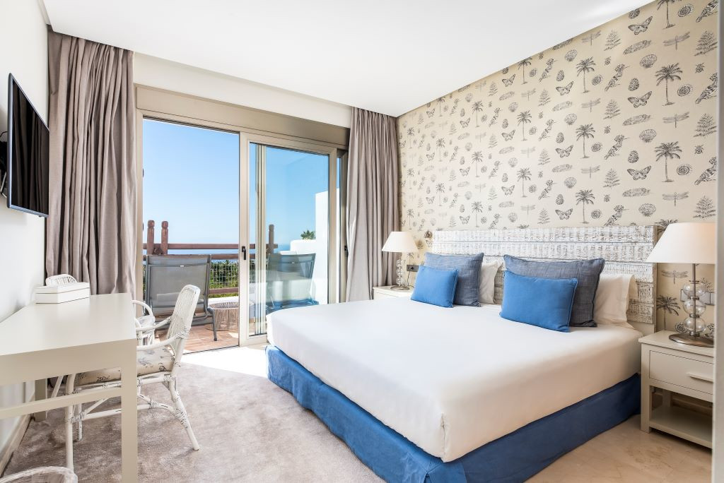 Bedroom with large bed, patterned wall, two lamps, desk, and ocean-view balcony in Tenerife.
