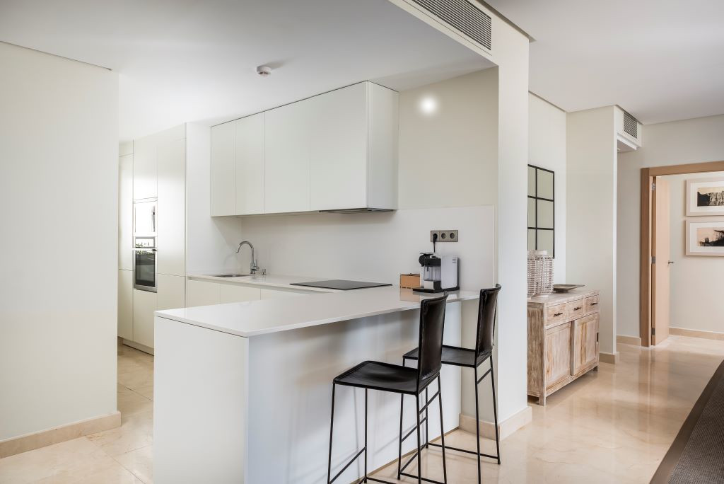 Modern kitchen in Tenerife apartment with white cabinets and two black stools.