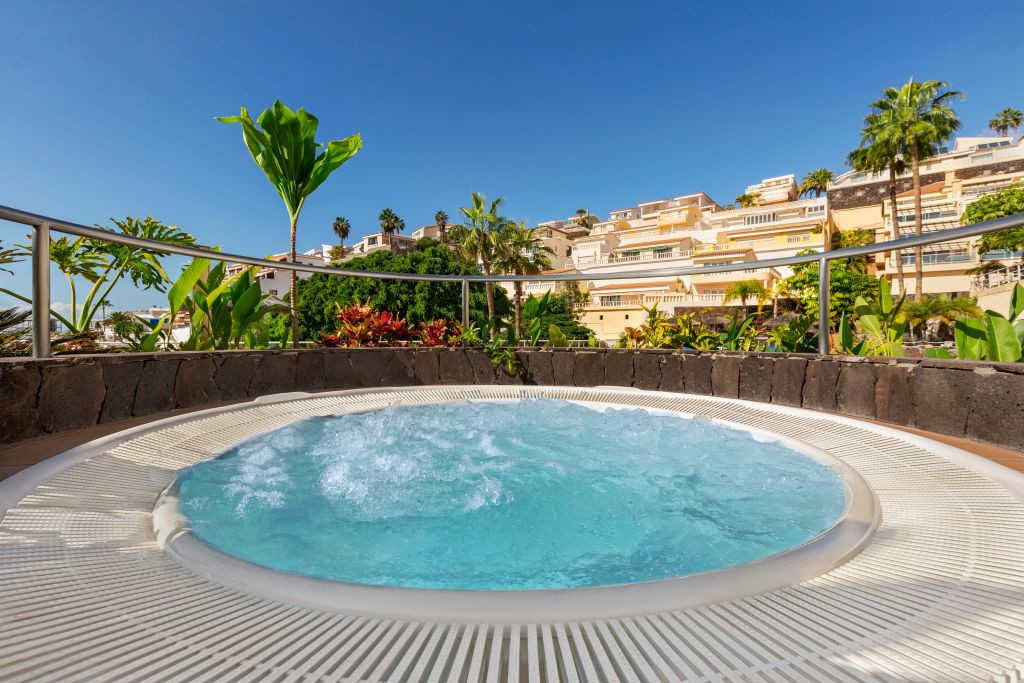 Jacuzzi surrounded by tropical plants with El Mirador apartments in Tenerife background.