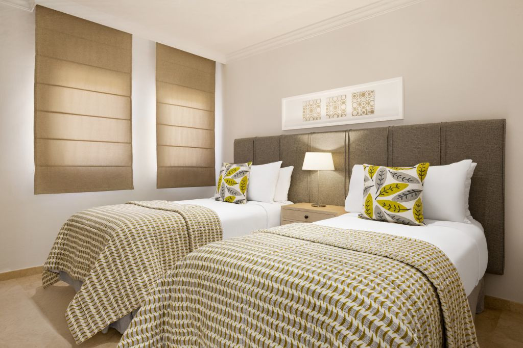 Two beds with patterned bedspreads, pillows, and a lamp in a Tenerife hotel room.