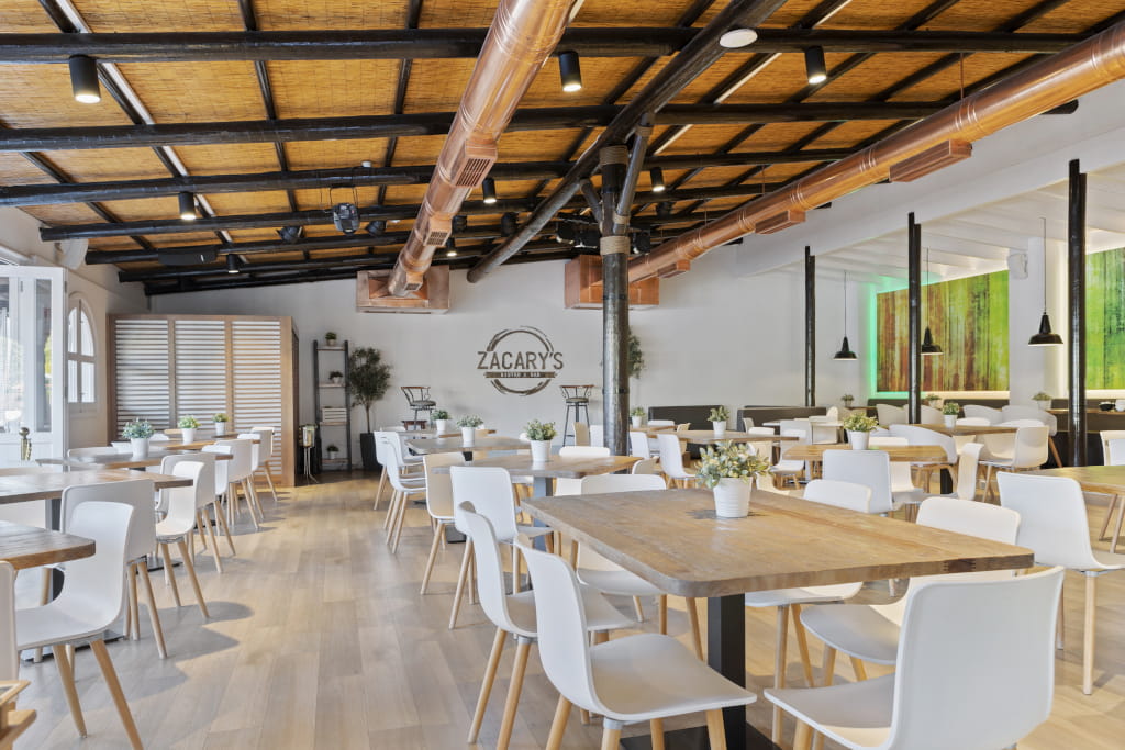 Spacious interior of Zacary's Bistro in Tenerife with wooden tables and white chairs.
