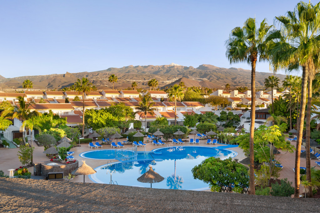 Hotel pool area with sunbeds and palm trees in Tenerife, mountains in the background.