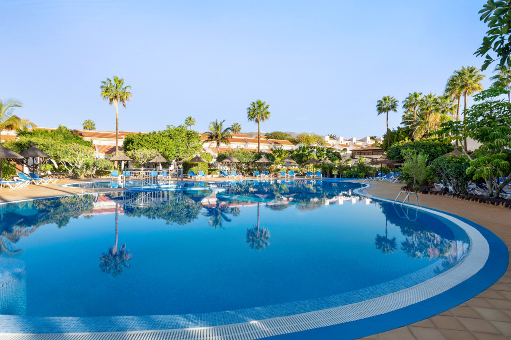 Outdoor swimming pool with loungers and palm trees at a Tenerife resort.