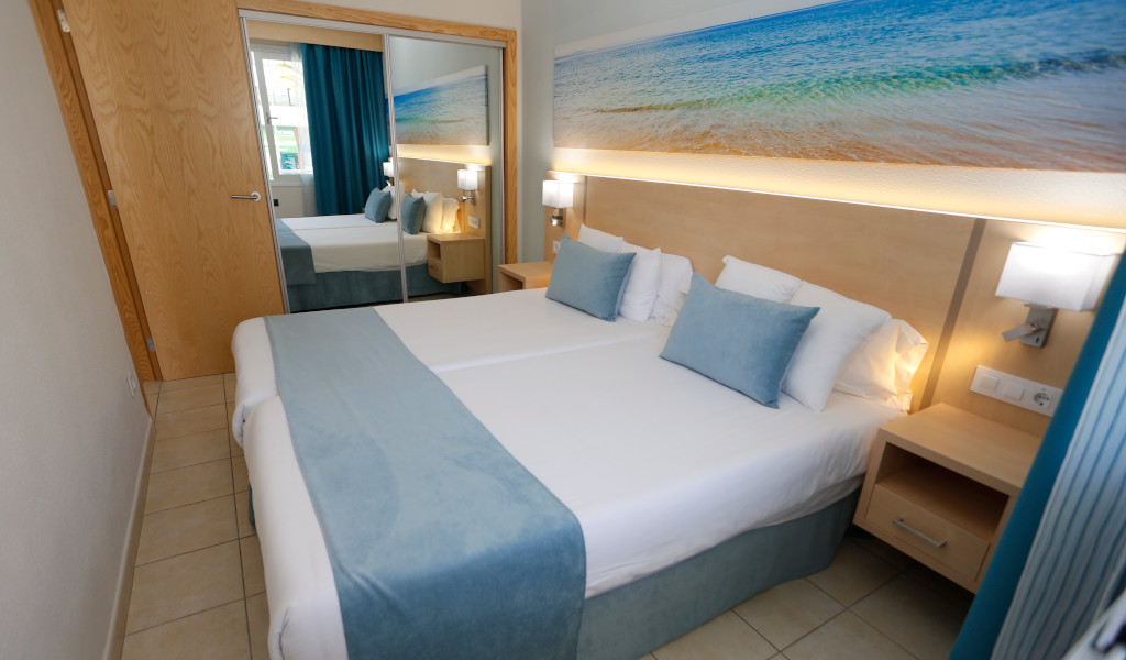 Double bed with blue accents in a Tenerife hotel room, large seascape artwork above.