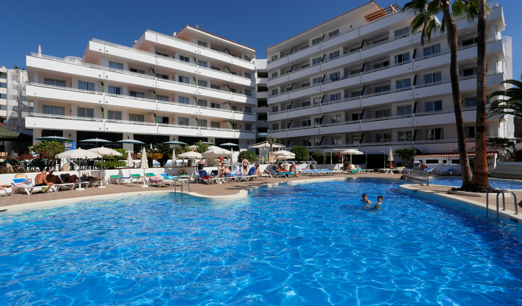 Outdoor swimming pool and sunbeds at a Tenerife hotel with people sunbathing.