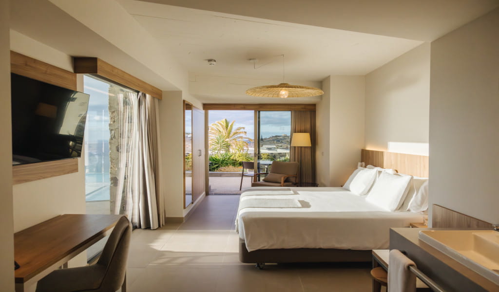 Modern hotel room with king bed, desk, and large window overlooking a terrace in Tenerife.