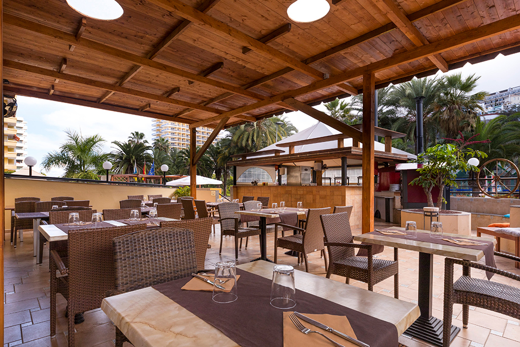 Outdoor restaurant seating area with wooden roof and palm trees in Puerto de la Cruz, Tenerife.