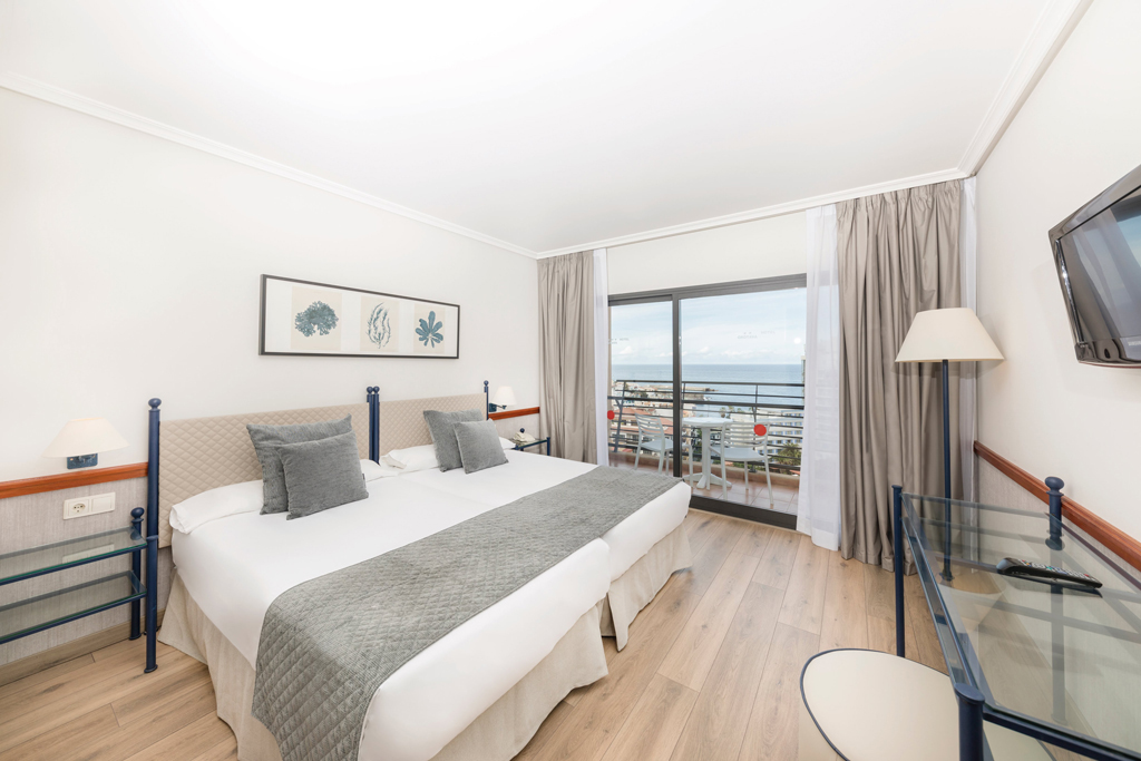 Hotel room in Tenerife with double bed, balcony view of ocean, and modern decor.