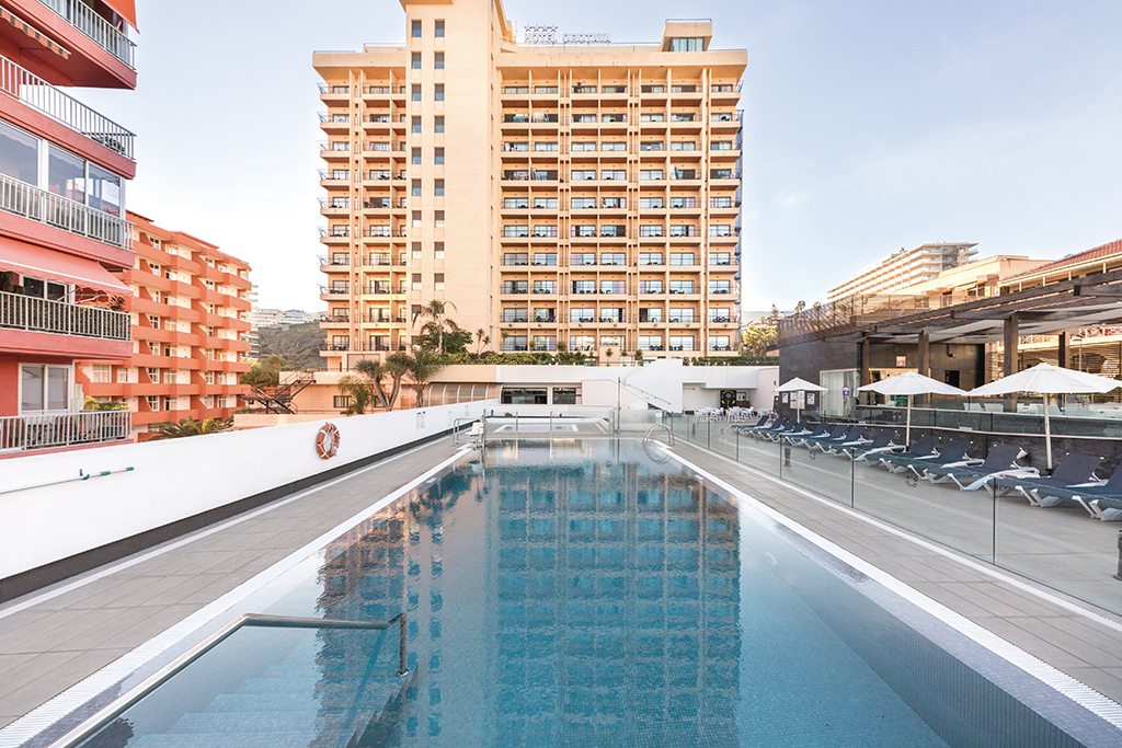 Outdoor pool area in Puerto de la Cruz with sun loungers and apartment buildings.