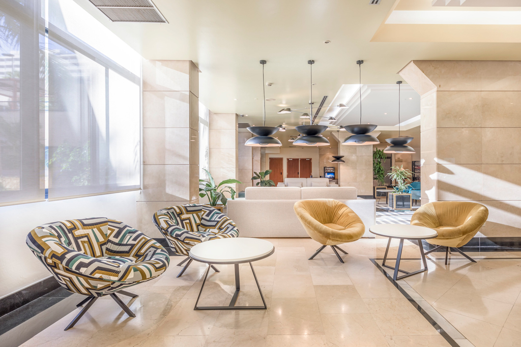 Lobby with patterned armchairs, round tables, and ceiling lights in a hotel in Tenerife.