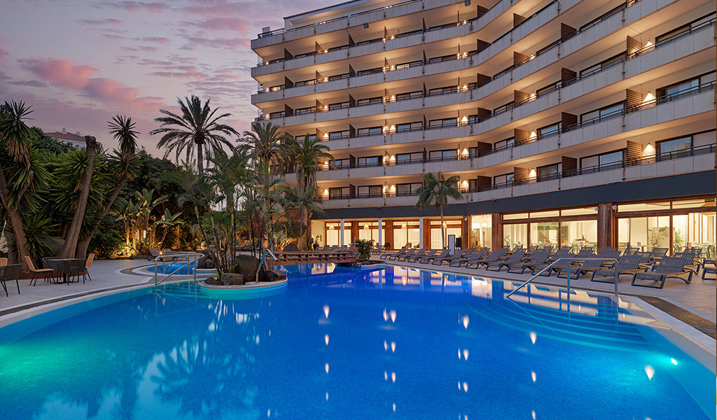 Outdoor pool and tall hotel building with palm trees in Tenerife.