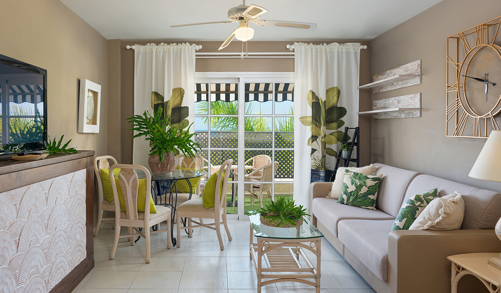 Living room with beige sofa, plants, glass table, and large wall clock in Tenerife.