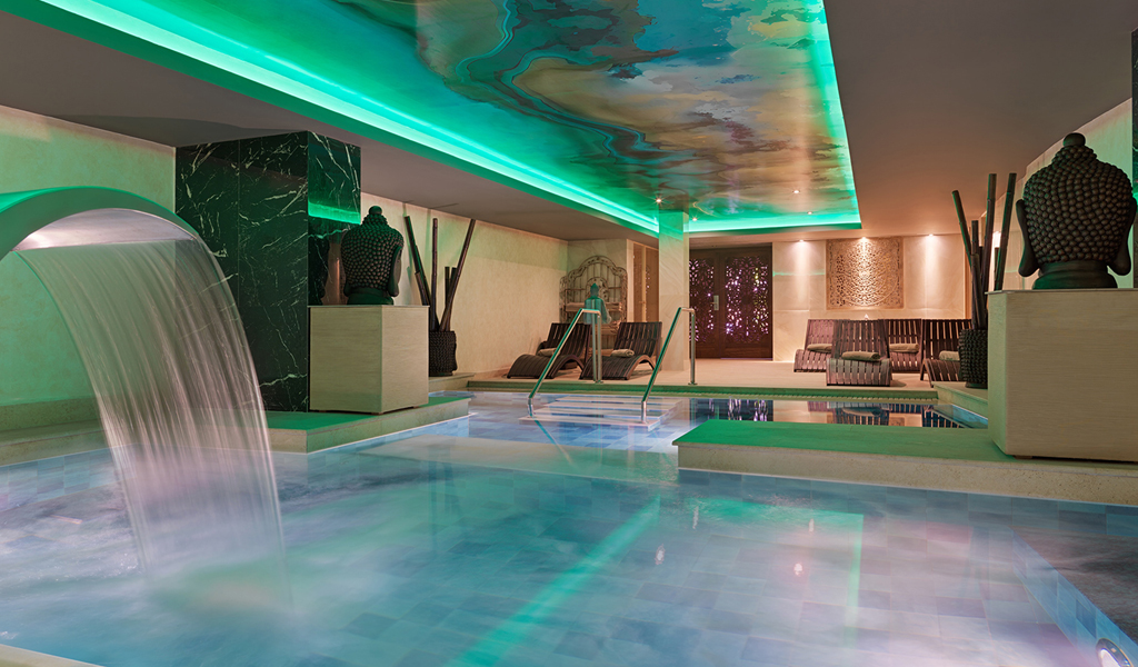 Indoor spa pool with waterfall feature, green lighting, and seating area in Tenerife.
