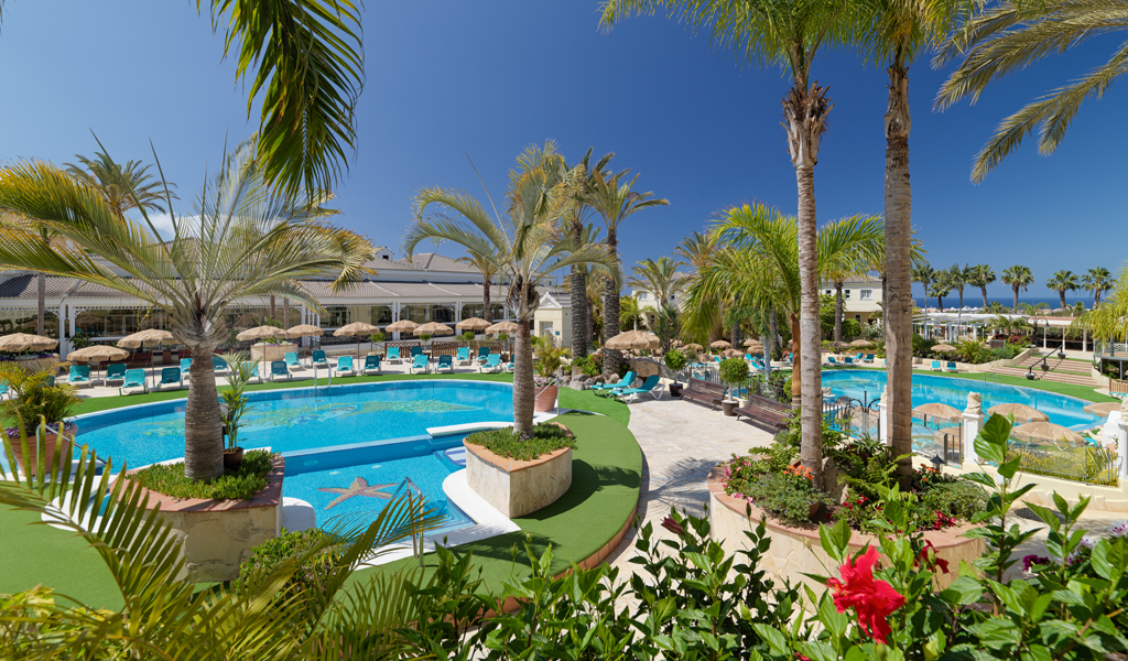 Outdoor pool area with palm trees and seating at a resort in Tenerife.