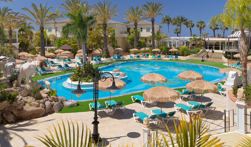 Outdoor pool area with palm trees and sunbeds at a Tenerife resort.