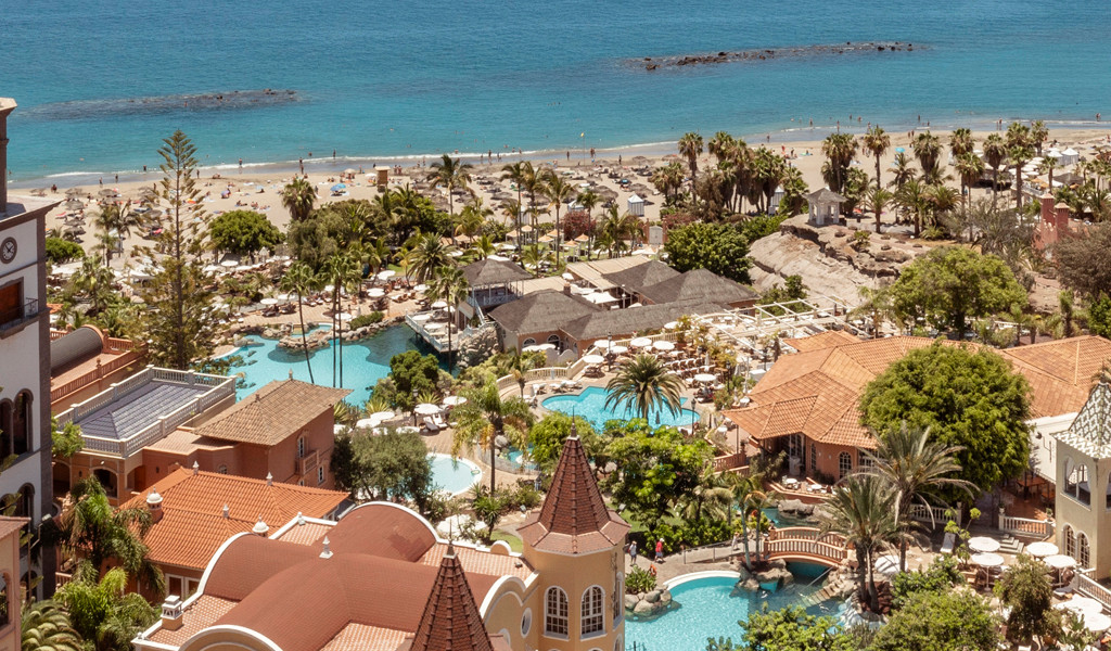 Beachfront resort in Tenerife with pools, palm trees, and nearby ocean.