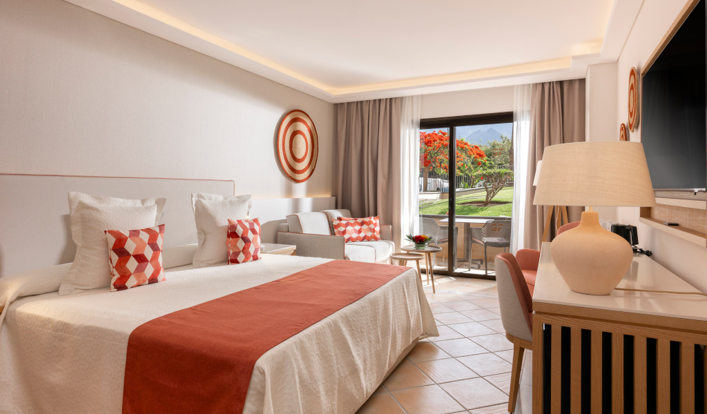 Hotel room with double bed, pillows, seating area, and garden view in Tenerife.