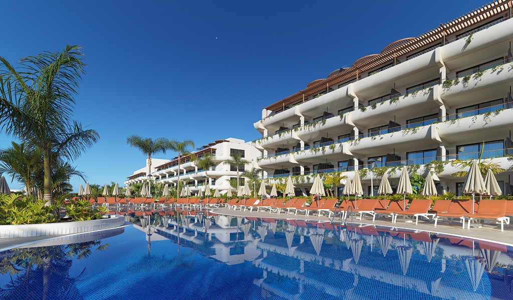 Hotel with pool and loungers in Tenerife under clear blue sky.