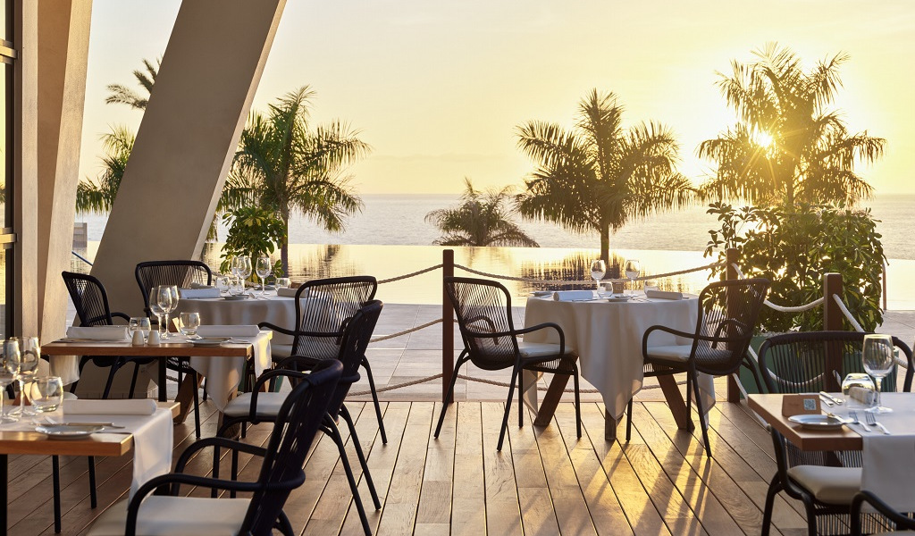 Outdoor dining area with tables, chairs, and ocean view at sunset in Tenerife.