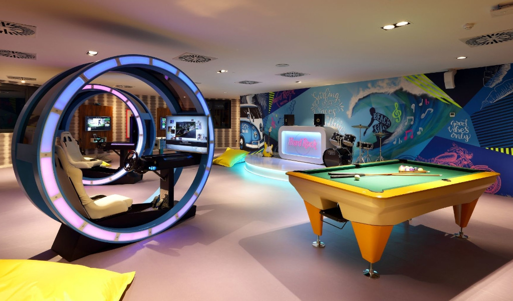 Gaming area with simulators, pool table, drum set, and Hard Rock glowing sign in Tenerife.