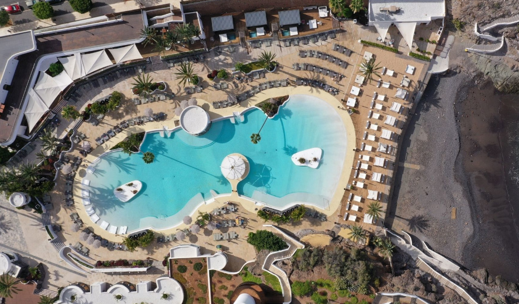Aerial view of a resort pool in Tenerife with surrounding loungers and beach.