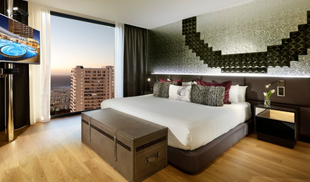 Hotel room with large bed, decorative wall, TV, and window view of Puerto de la Cruz, Tenerife.