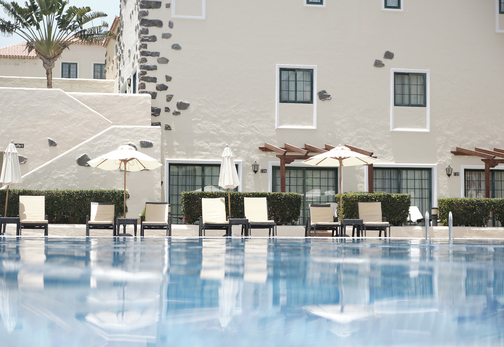 Sun loungers and umbrellas by a pool at a building in Tenerife.