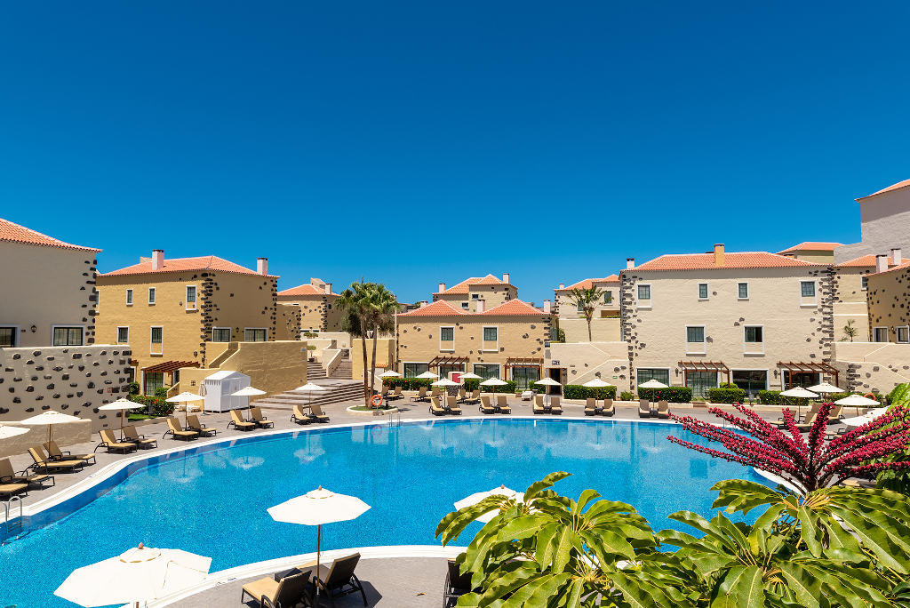 Outdoor pool surrounded by sun loungers and beige buildings in Tenerife.