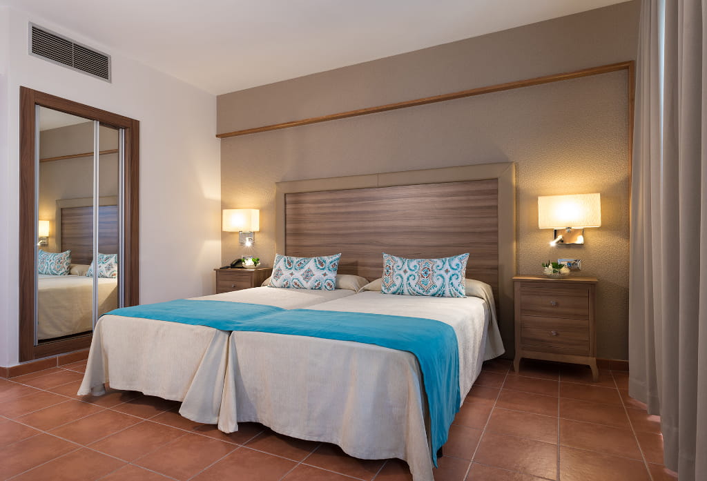 Two beds with blue blankets and pillows in a Tenerife hotel room.