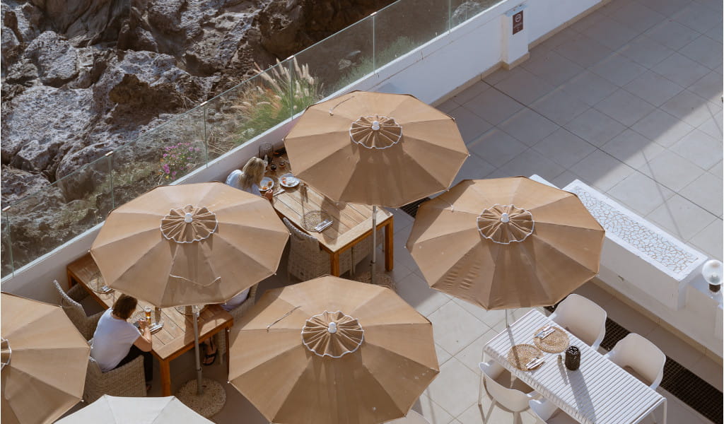 Outdoor terrace with tables, beige umbrellas, and people dining in Tenerife.