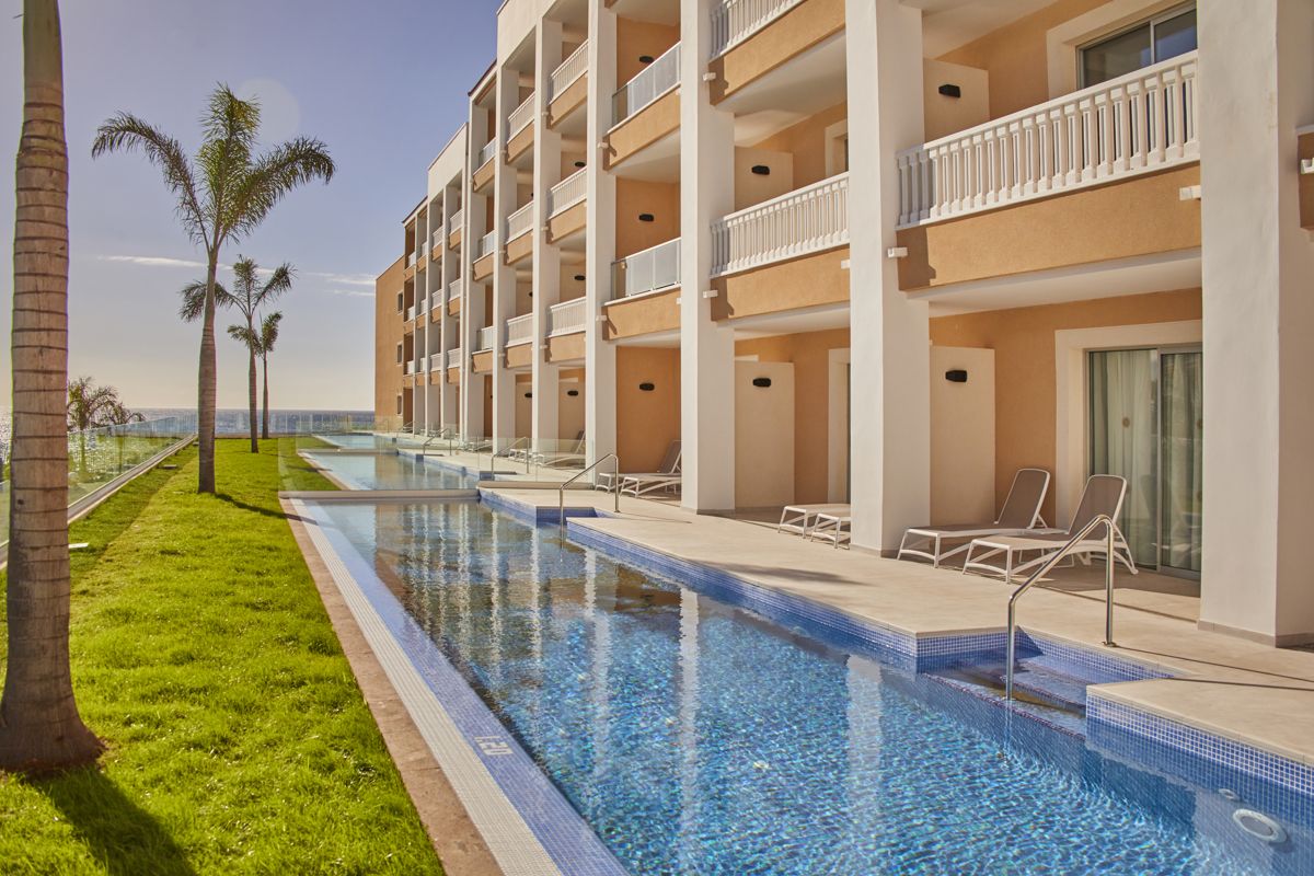 Hotel poolside view at a resort in Tenerife with sun loungers and palm trees.