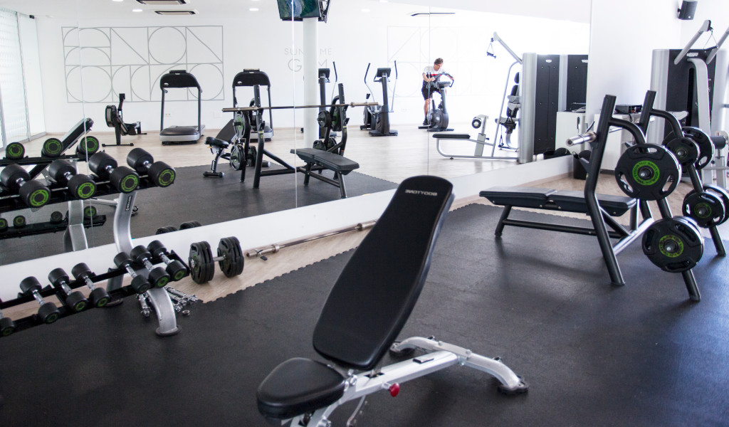 Gym in Tenerife with weights, treadmill, bench, and a person on an exercise bike.