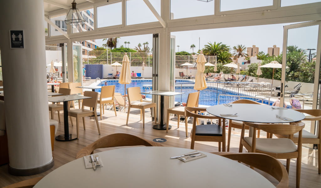 Dining area with pool view in Tenerife hotel. People relaxing on sunbeds.