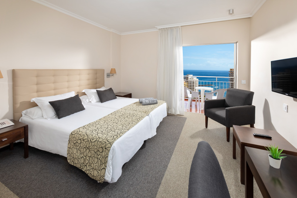 Comfortable hotel room with sea view in Tenerife, featuring a double bed, chair, and TV.