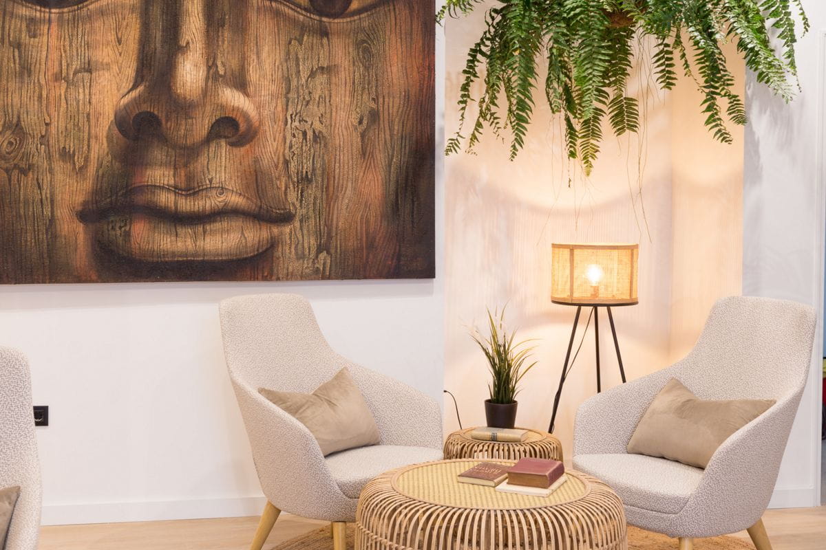 Seating area with two chairs, a wooden table, lamp, and a Buddha face artwork in Tenerife.