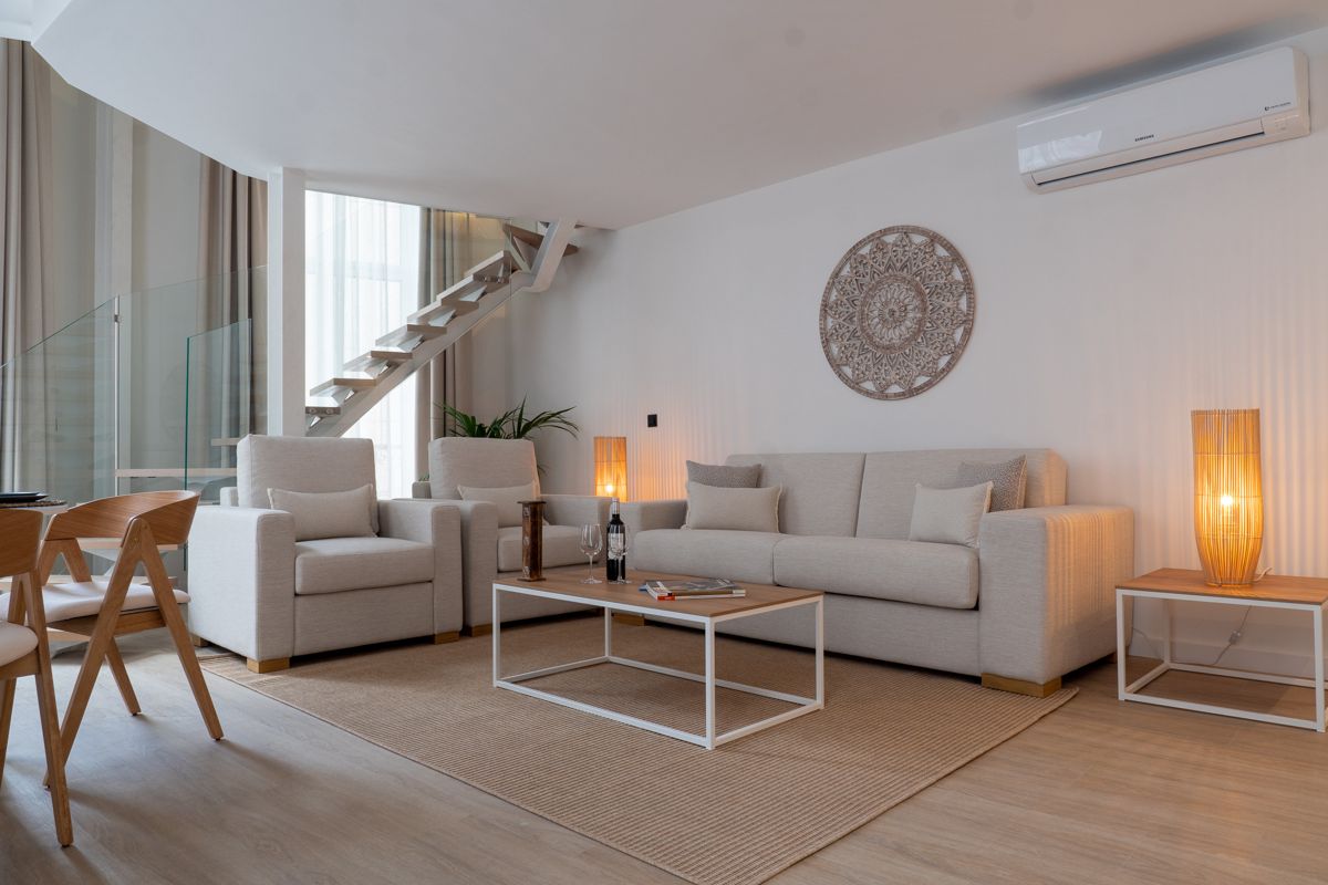 Modern living room with beige sofas, coffee table, and staircase in Tenerife.