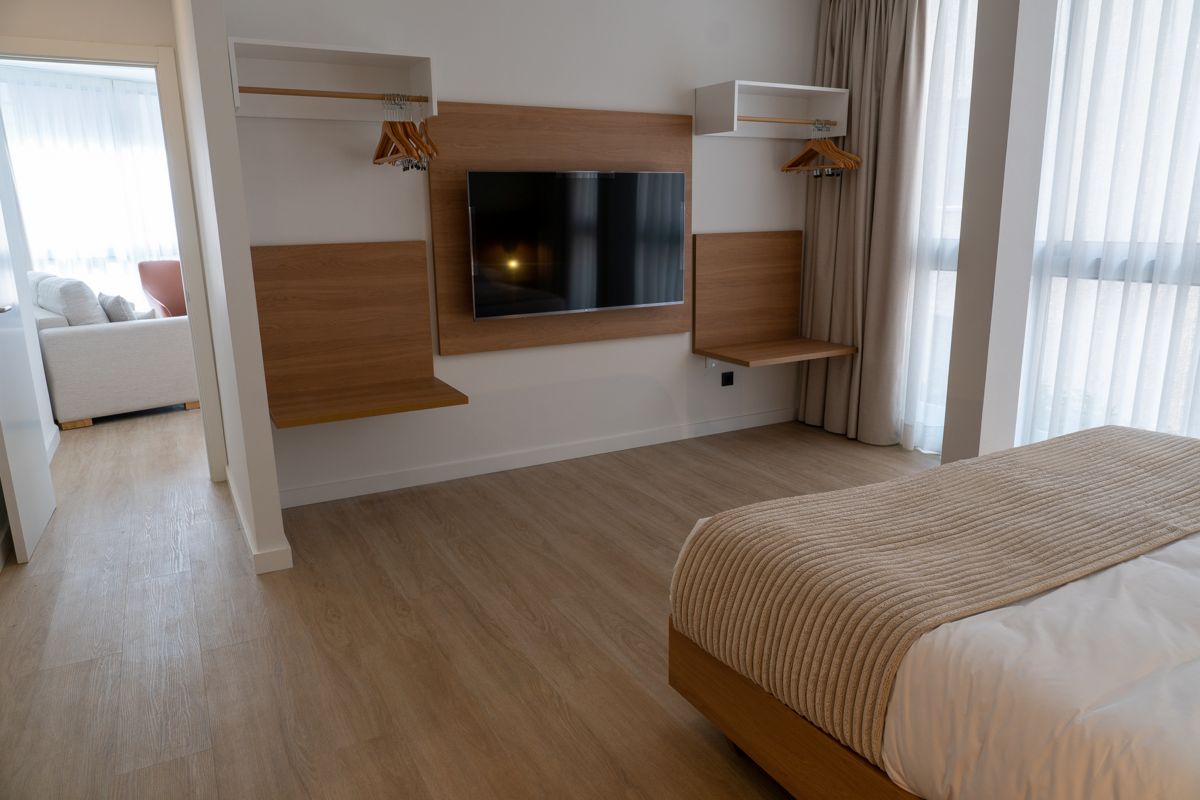 Bedroom with a mounted TV, wooden shelves, and view into sitting area in Tenerife.