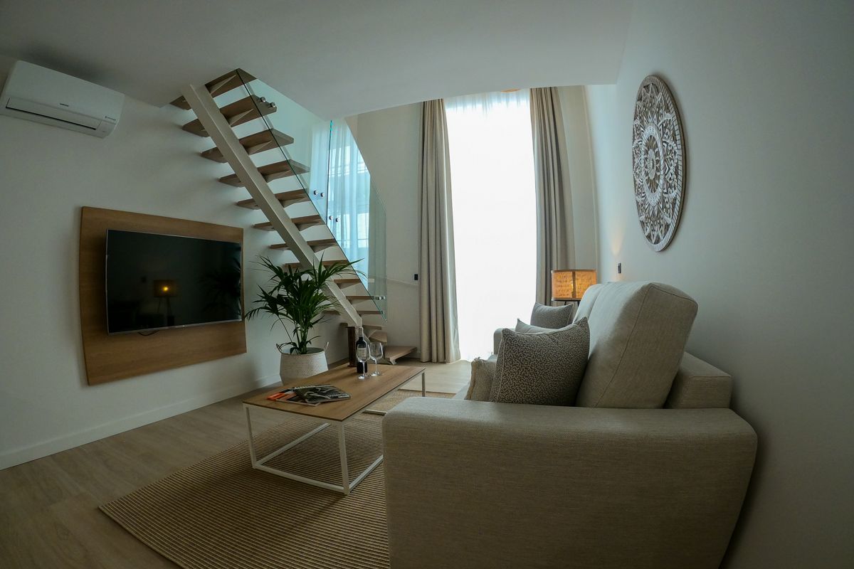 Living room in a Tenerife apartment with sofa, TV, and wooden stairs.
