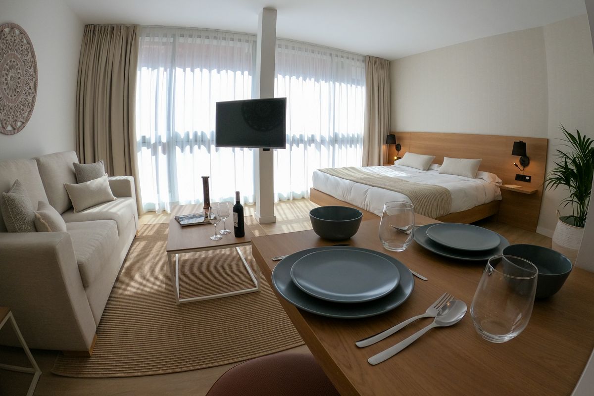 Modern apartment living area with sofa, bed, table set, and window view in Tenerife.